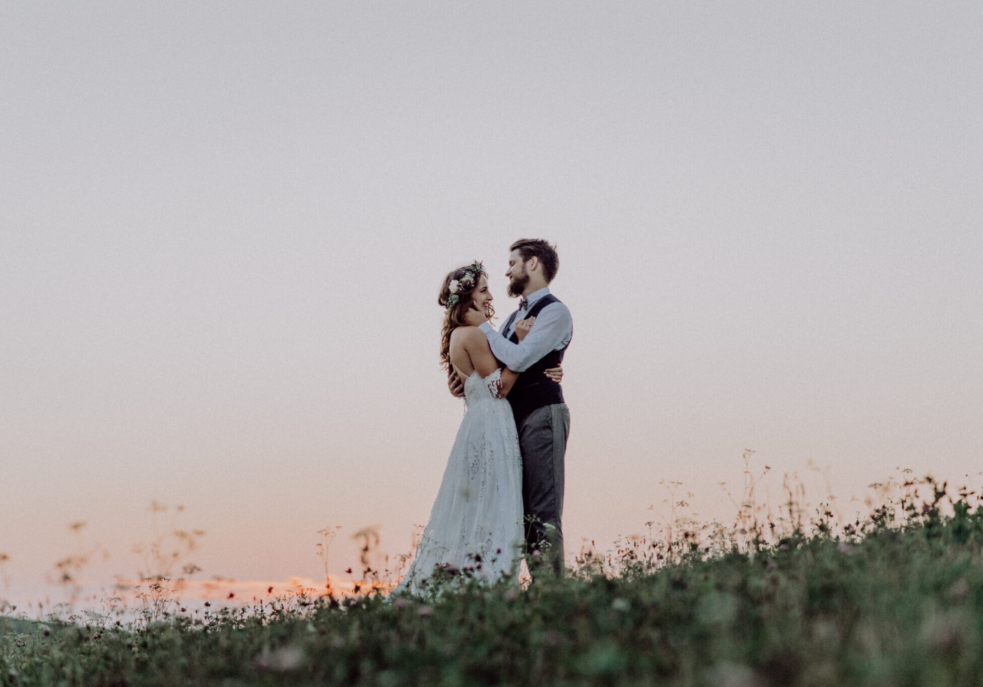 Young bride and groom outside in green nature at romantic sunset, hugging.